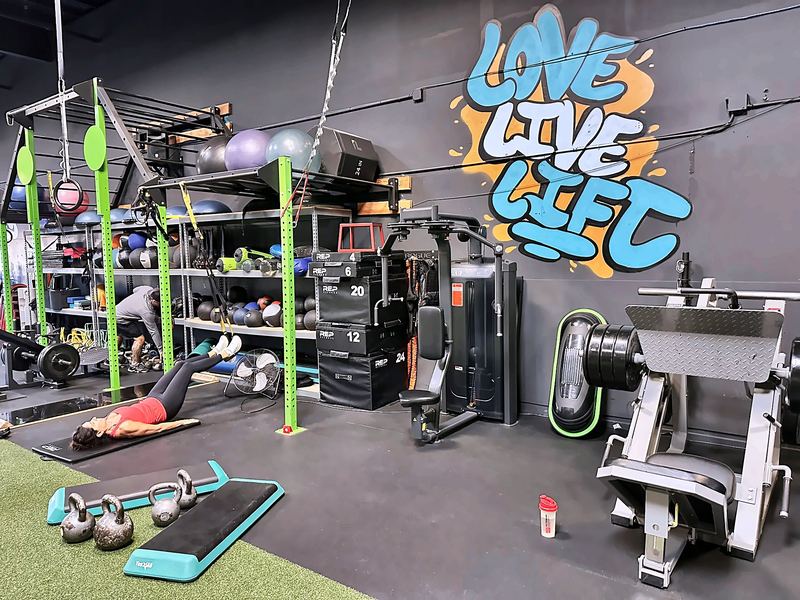Gym area with racks and a leg press in front of a graffiti-style "Live Love Lift" wall mural.