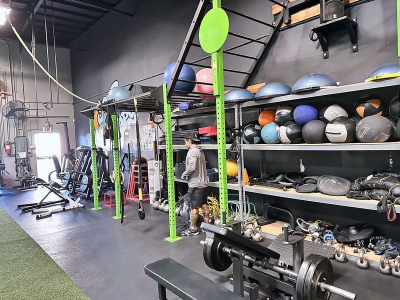 Racks, benches and a shelf of medicine balls and kettlebells with green support posts.
